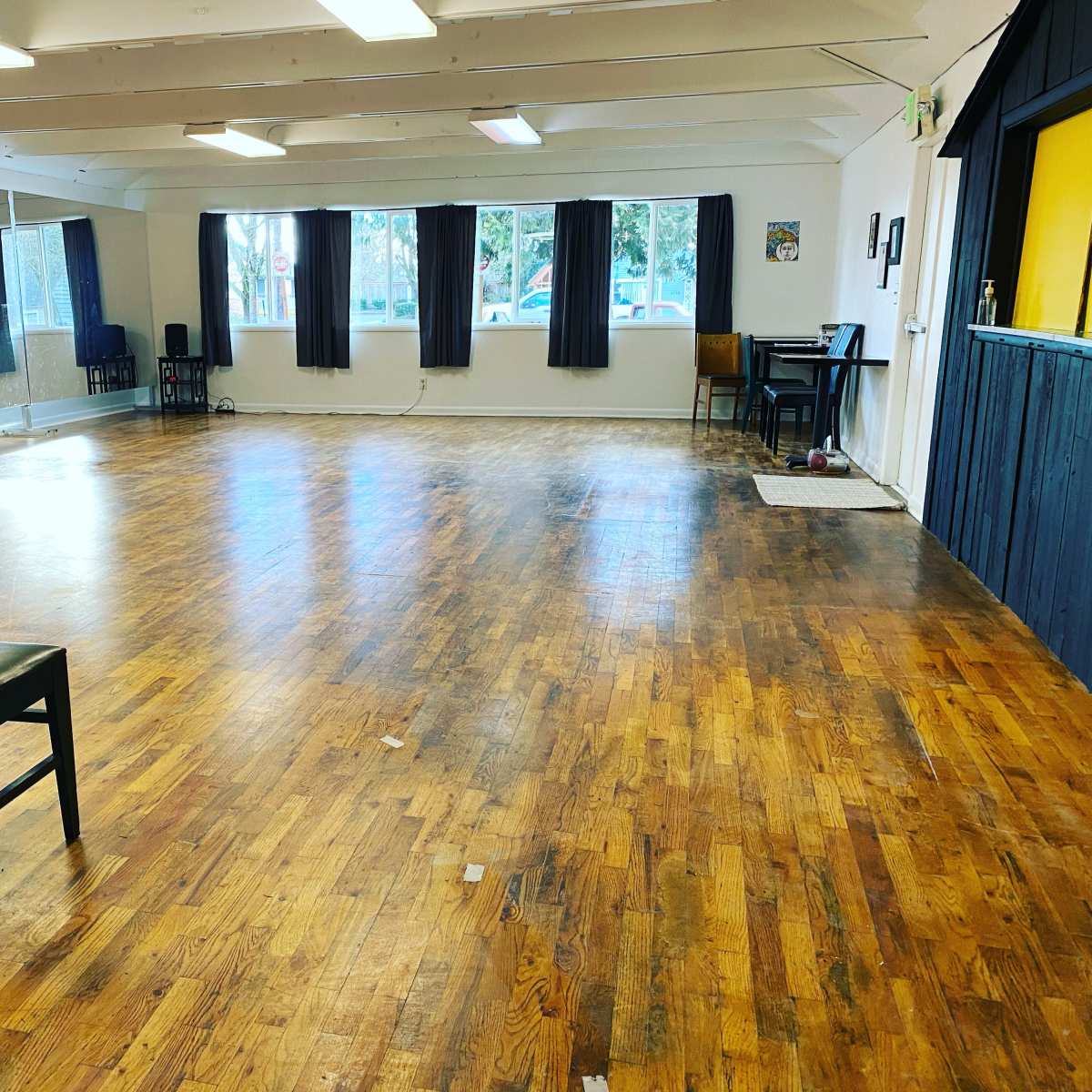 A spacious dance studio with wooden floors, mirrors on one wall, and several windows allowing natural light.