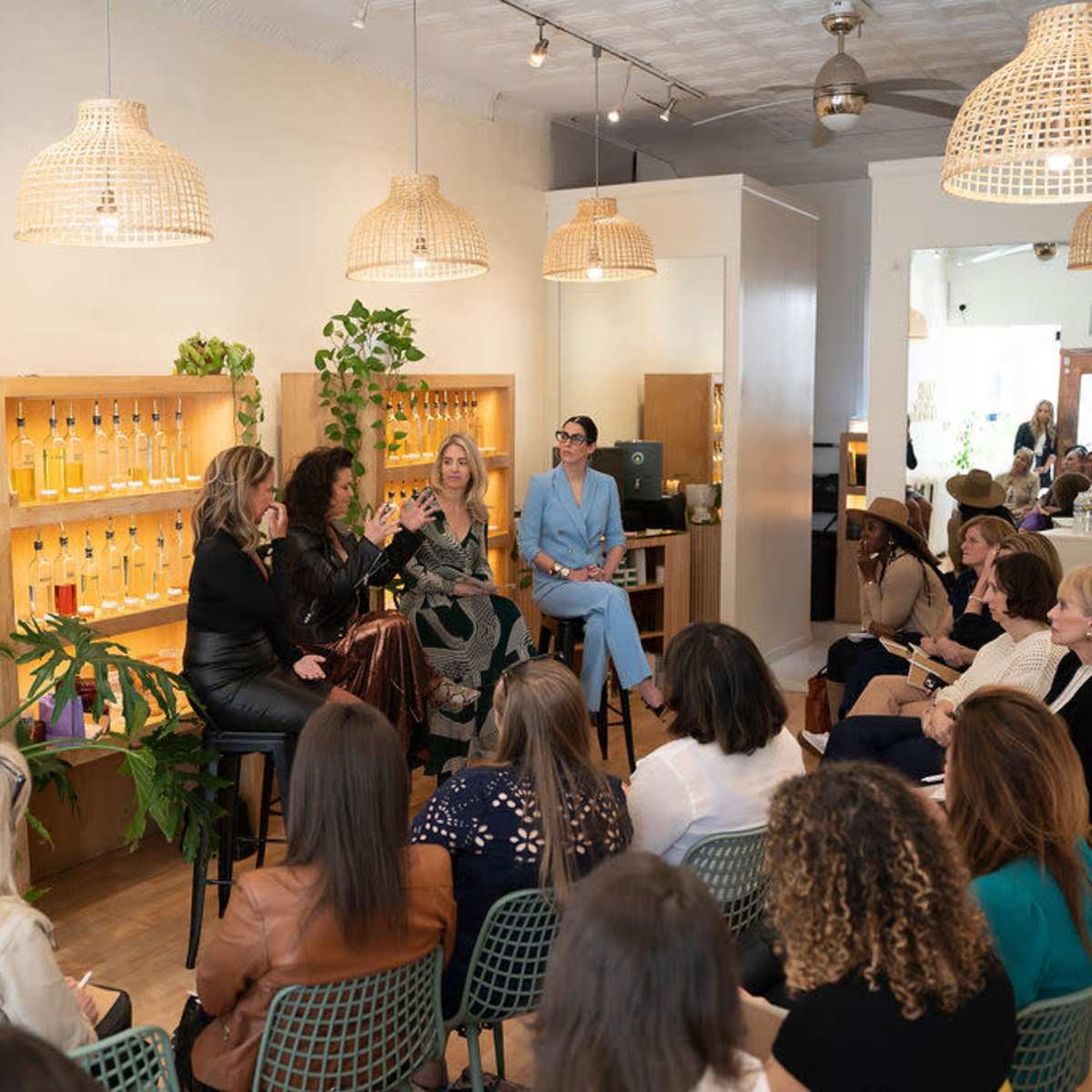 A group of women participates in a panel discussion in a bright, airy room filled with plants and shelves of products.