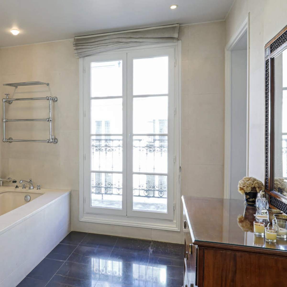The bathroom features a freestanding bathtub, a wall-mounted towel rack, and a wooden vanity, with large windows providing natural light.