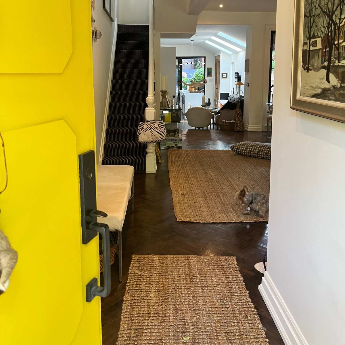 A bright yellow door provides a view into a cozy interior hallway that leads to a staircase and an adjacent living area.
