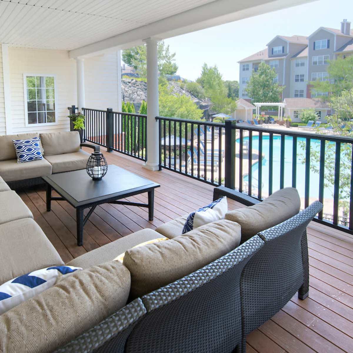 A spacious balcony features a sectional sofa arranged around a black coffee table, overlooking a swimming pool and landscaped area.