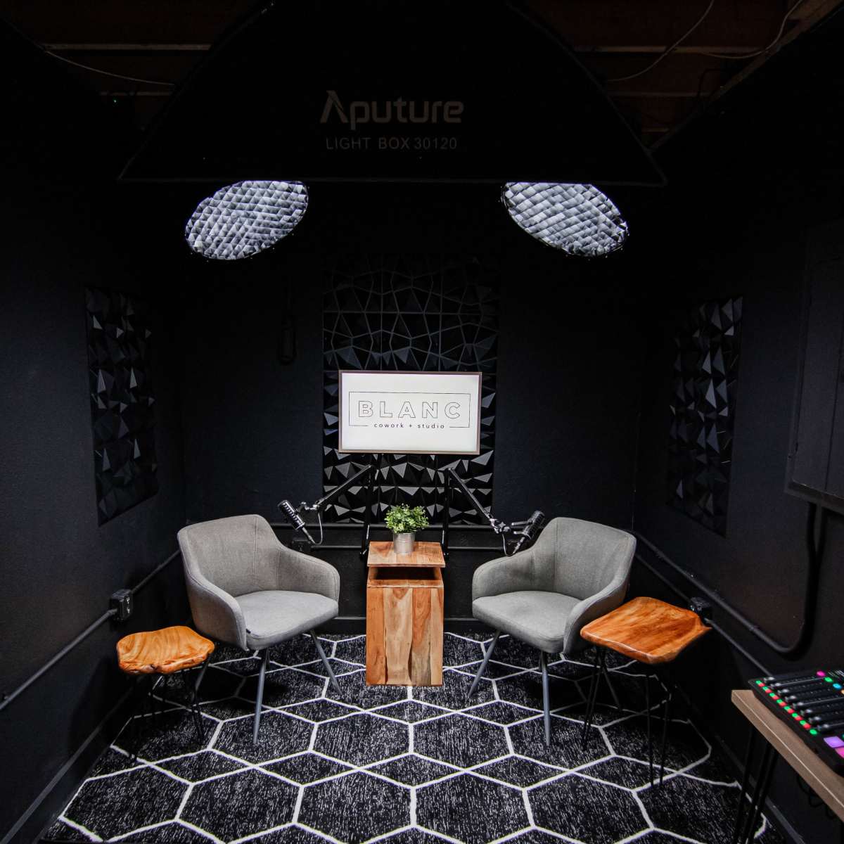 A small room with two gray chairs, a wooden table between them, and decorative wall panels, illuminated by overhead lights.