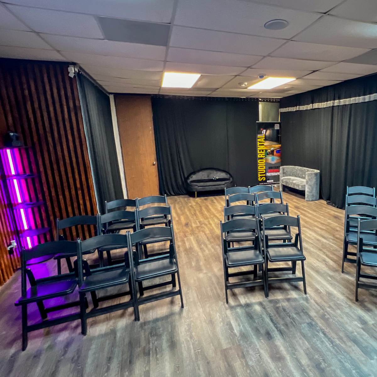 An empty room with black chairs arranged in rows, a couch in the background, and black curtains hanging on the walls.
