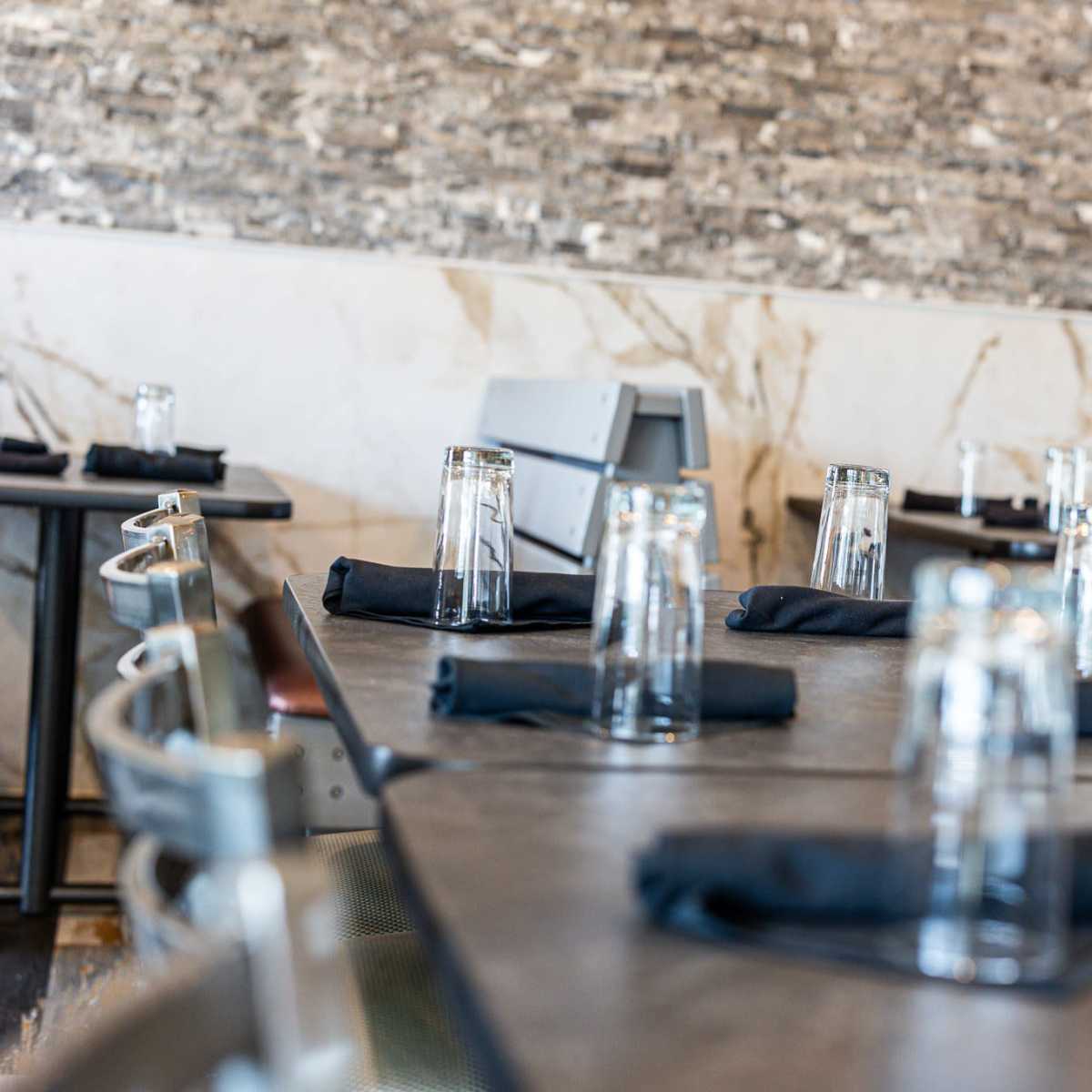 A restaurant interior with tables set with black napkins and empty glassware.