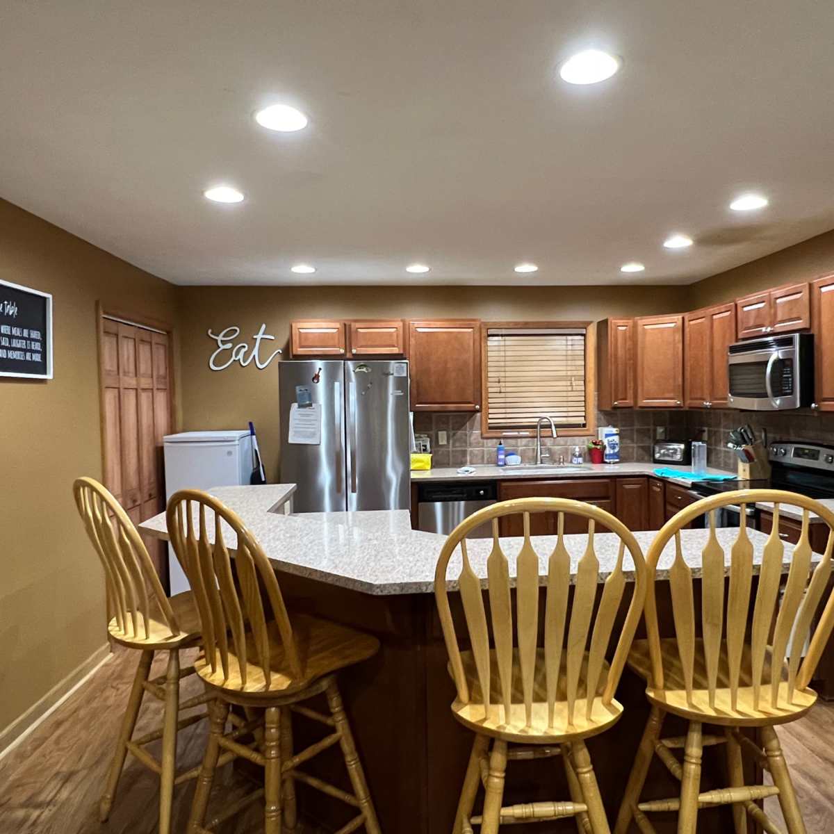 The kitchen features wooden cabinets, stainless steel appliances, and a large island with four wooden bar stools.