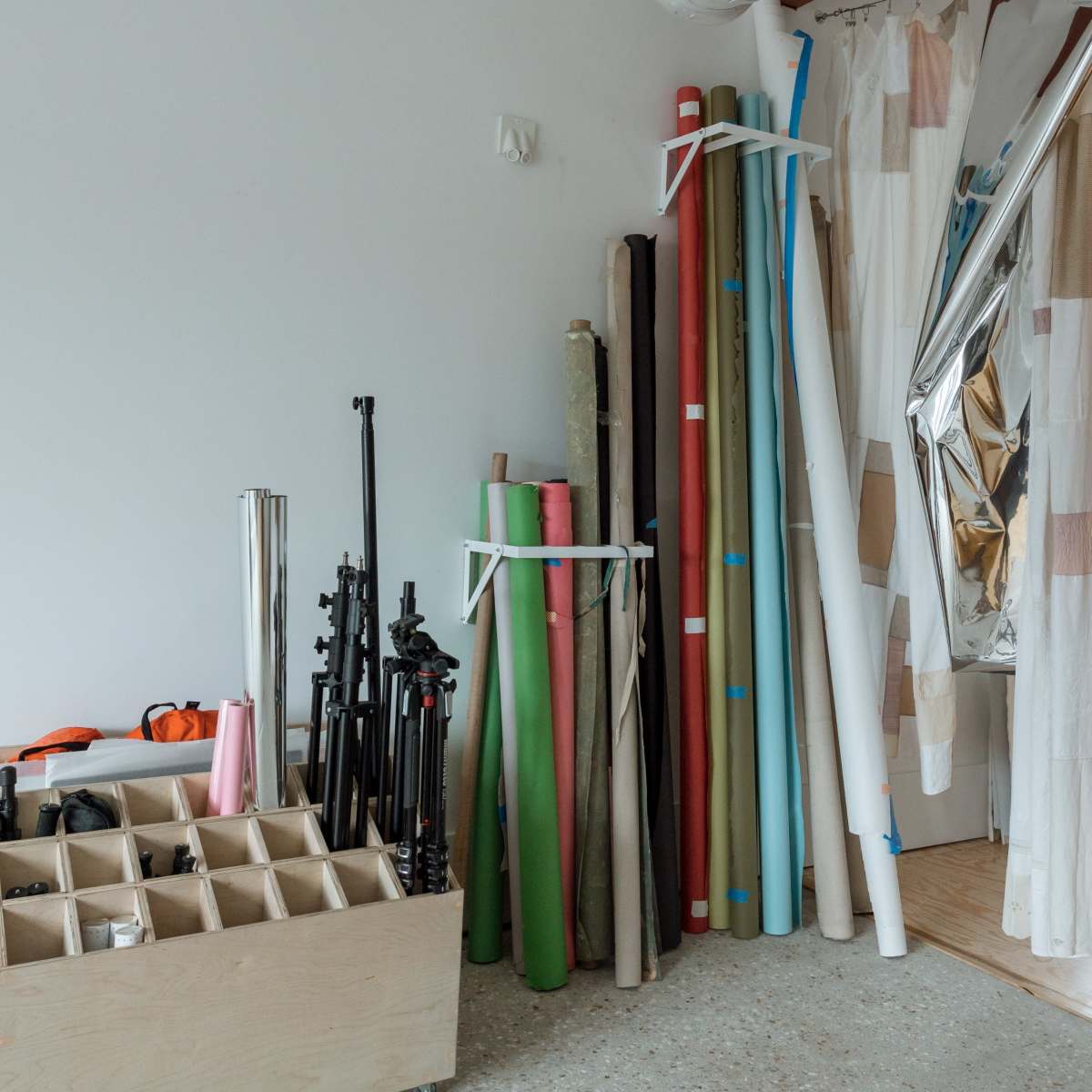 A storage area features various rolls of colored paper and equipment, organized against a wall in a studio space.