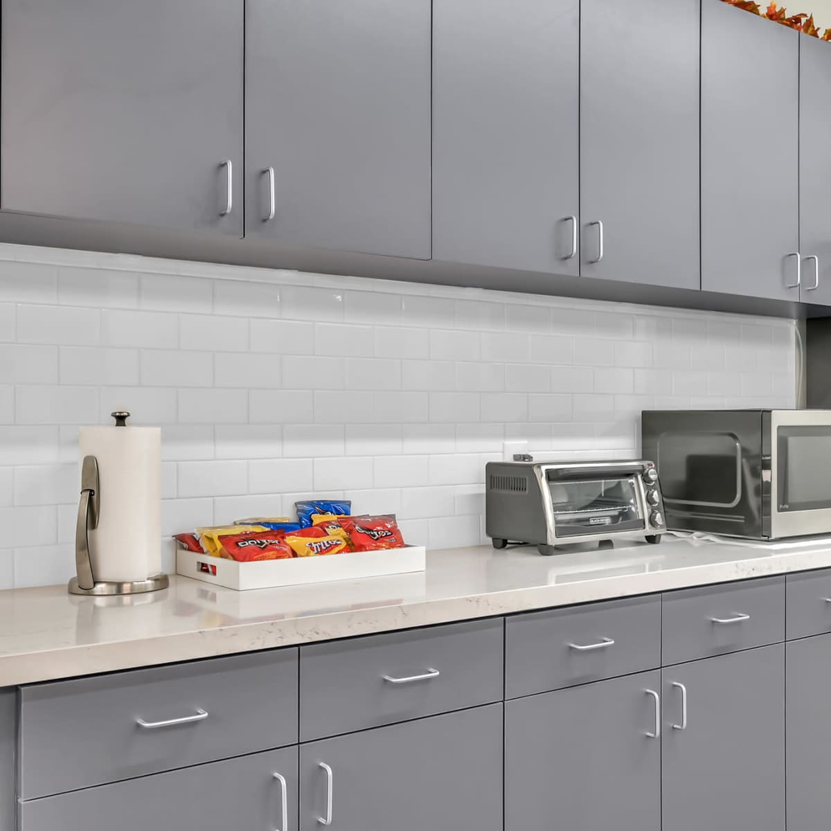 A modern kitchen with gray cabinets, a refrigerator, a microwave, and a countertop displaying a tray of snacks.