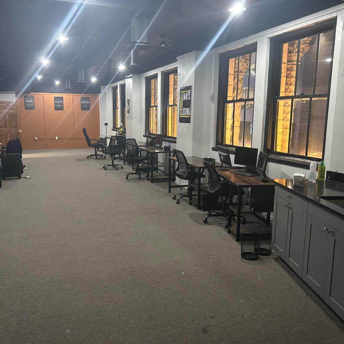 A large, empty office space with several desks, computers, and illuminated windows.