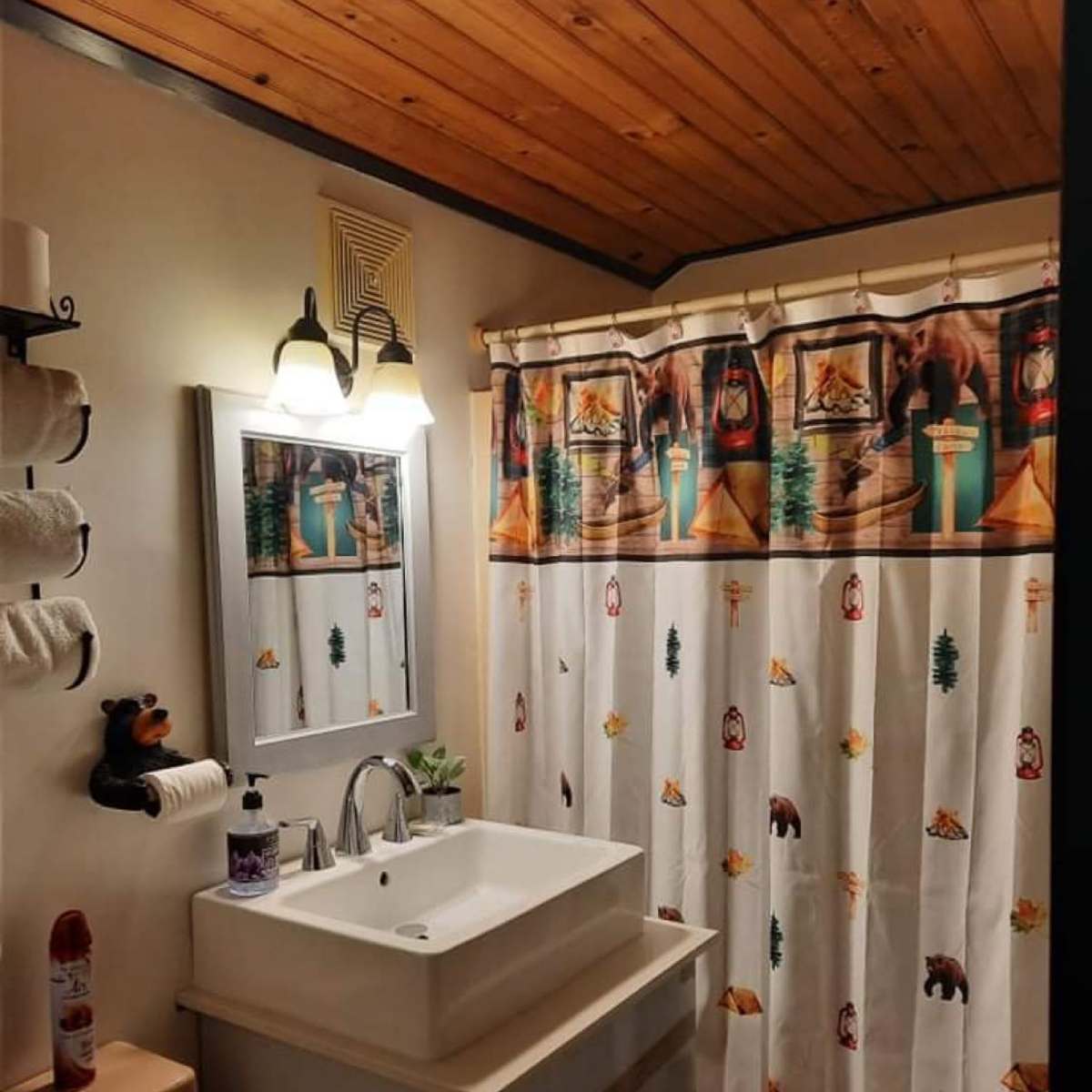The bathroom features a wooden ceiling, a modern sink with a sleek design, and a shower curtain adorned with a wildlife and camping theme.