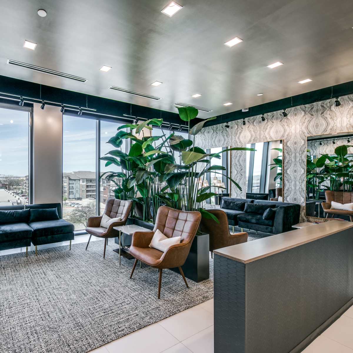 A modern lounge area with large windows, contemporary furniture, and indoor plants.