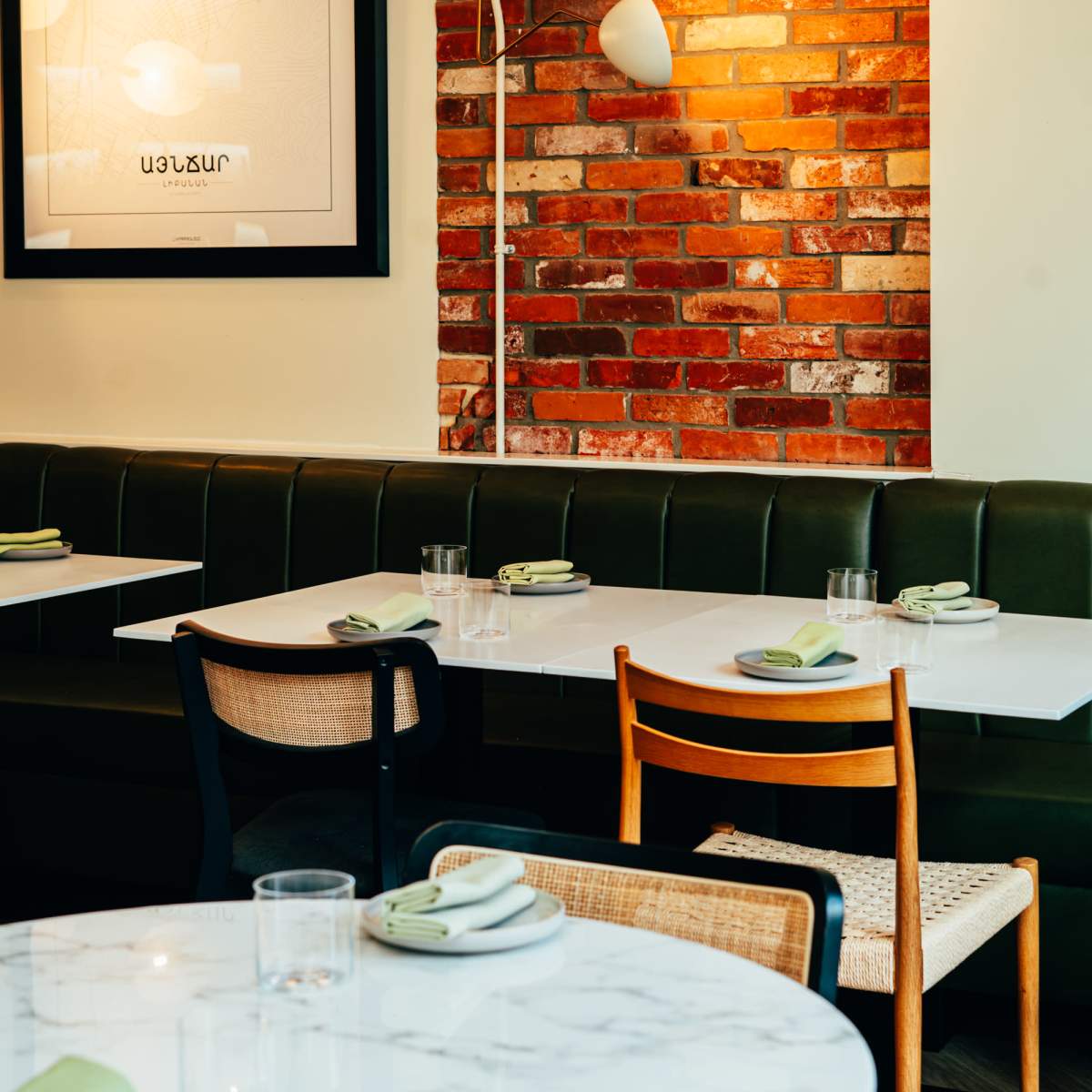 A modern restaurant interior with green upholstered seating, wooden chairs, and white tables set with napkins and glassware.
