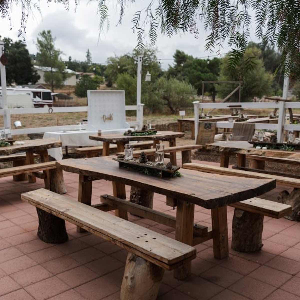 A rustic outdoor seating area with wooden tables and benches set on a tiled patio.