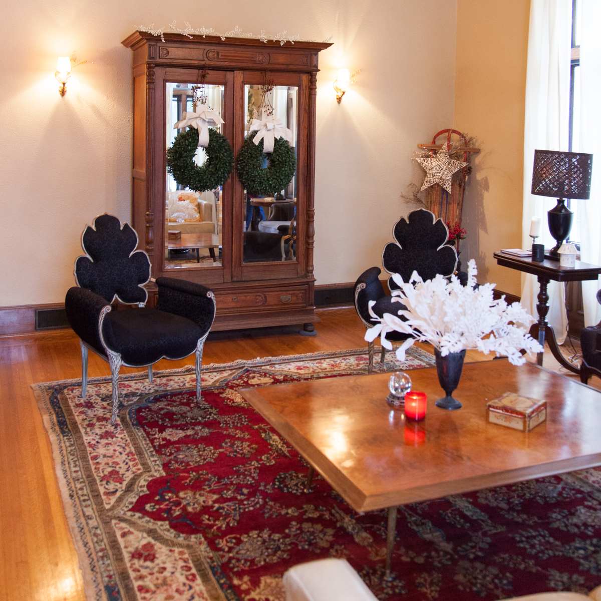 A cozy living room featuring ornate furnishings, a decorative area rug, and a vintage cabinet adorned with Christmas wreaths.