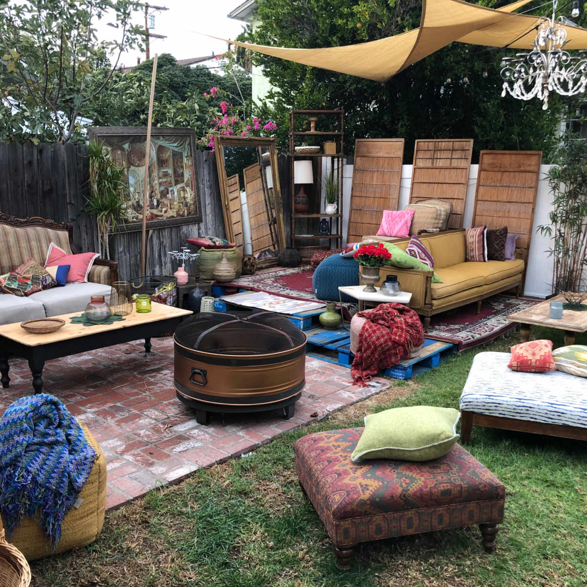 A cozy outdoor living space featuring a mix of seating options, colorful cushions, a fire pit, and decorative elements under a shaded canopy.