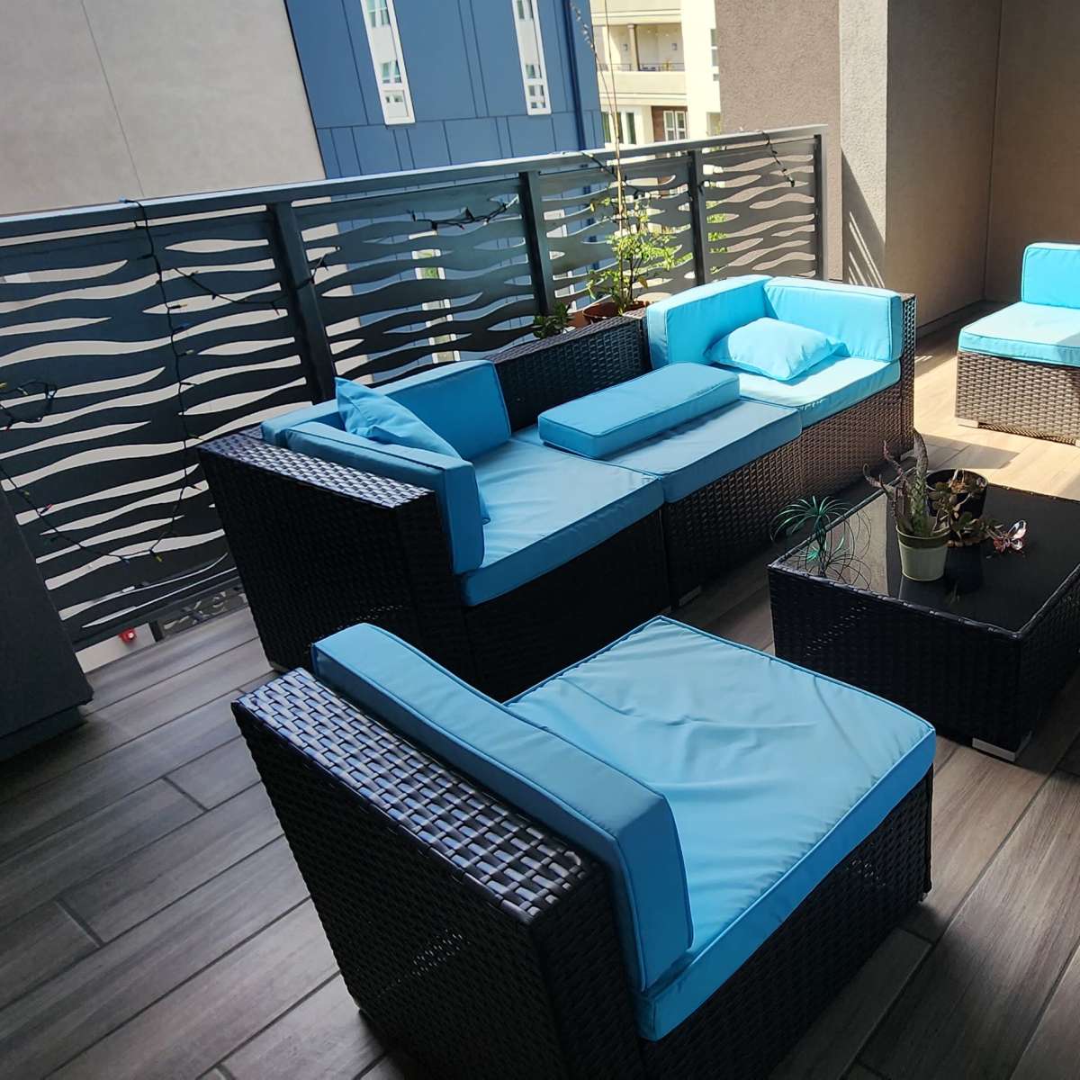 A modern balcony features wicker furniture with light blue cushions and a small potted plant on a table.
