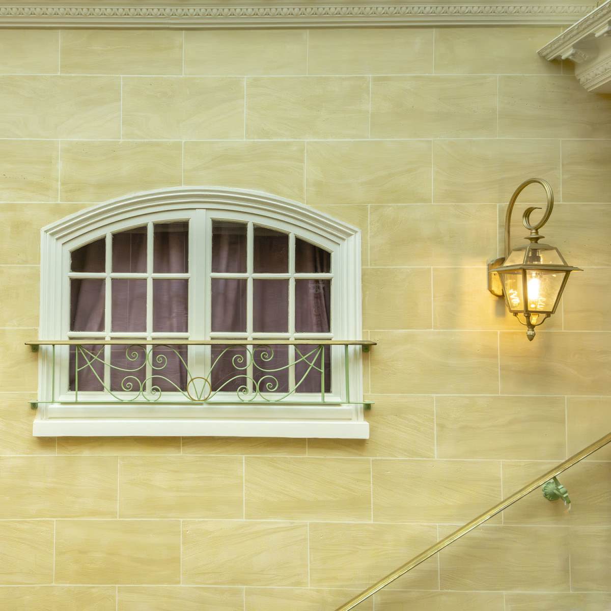 A decorative arched window framed by two wall-mounted lanterns, set against a light-colored stone wall.