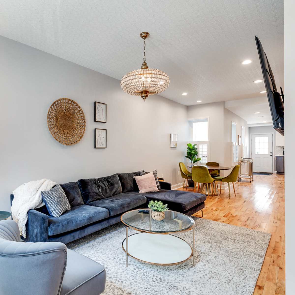A modern living room with a blue sectional sofa, a glass coffee table, and a stylish chandelier, all set against a light gray wall.
