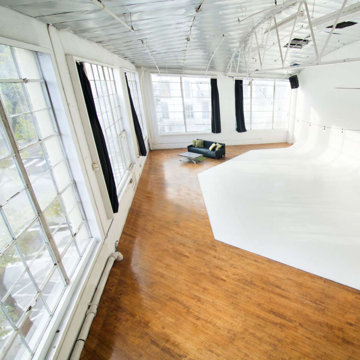 A spacious studio with large windows, a smooth white backdrop, wooden flooring, and a minimalist seating area.