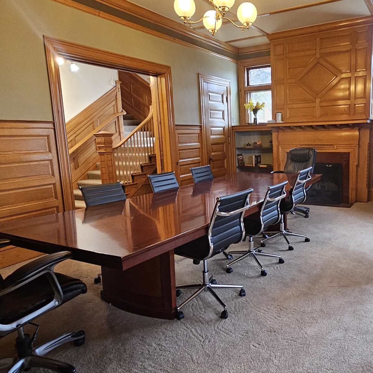 A conference room features a large wooden table surrounded by black chairs, with wooden paneling and a fireplace along one wall.