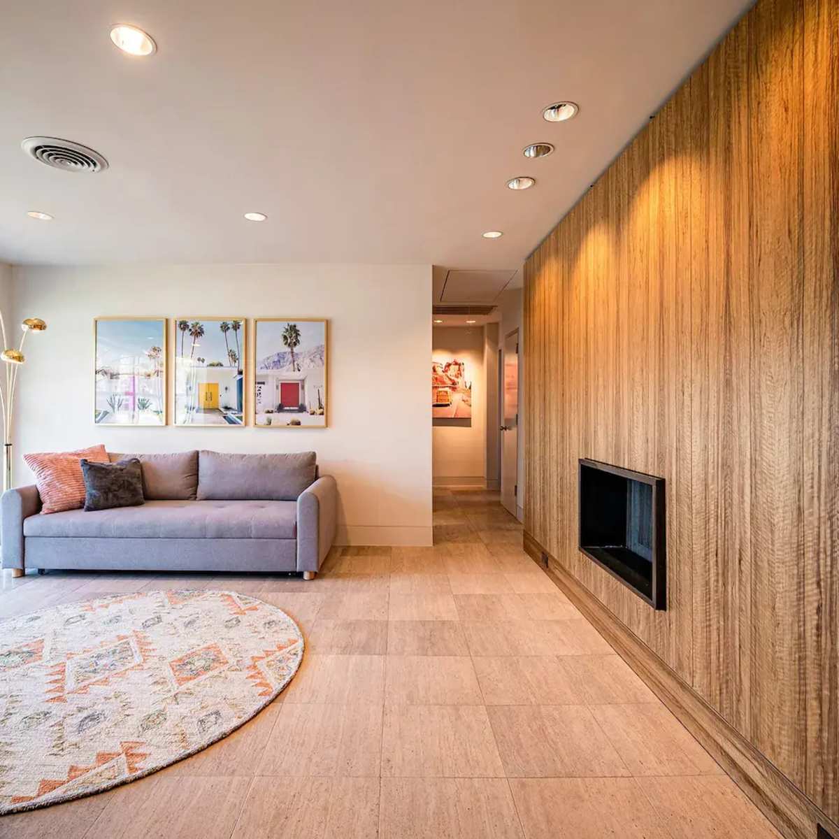 A modern living room with a gray sofa, a round area rug, two framed pictures on the wall, and a warm wooden accent wall.