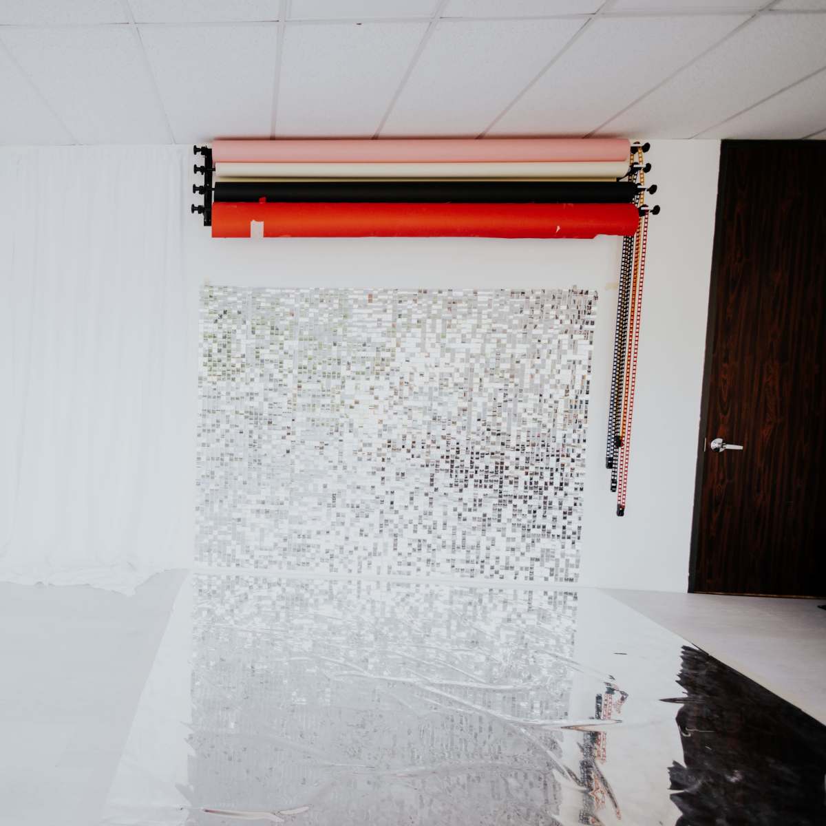An interior room with white drapery, a shiny silver backdrop, and colorful rolled paper at the top.