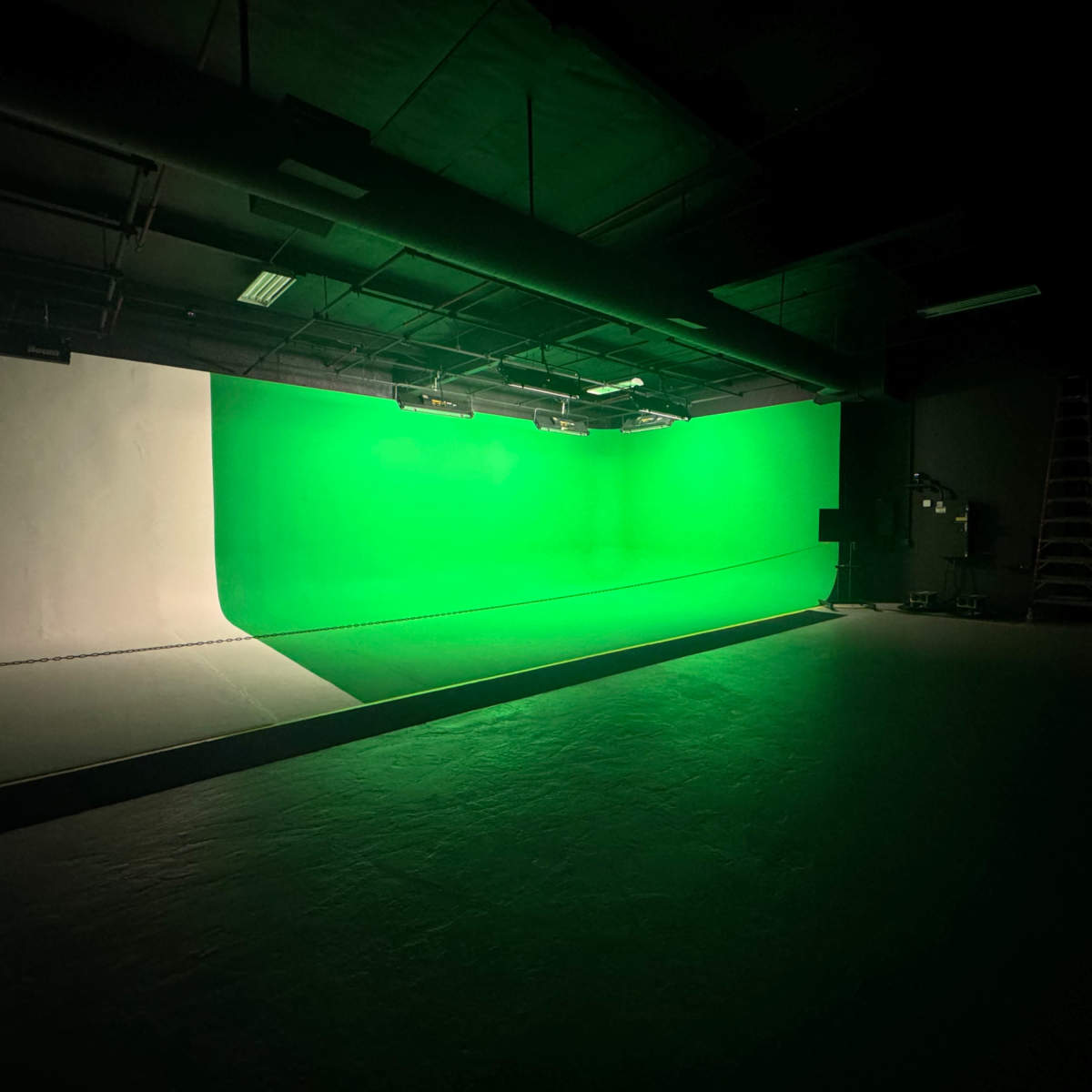 A studio with a green backdrop illuminated by overhead lights in a dimly lit environment.