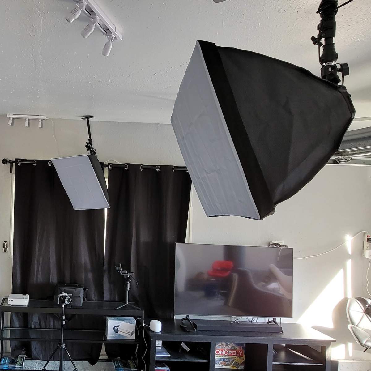 A modern living room setup featuring a large flat-screen TV, black curtains, a projector screen, and softbox lighting equipment.