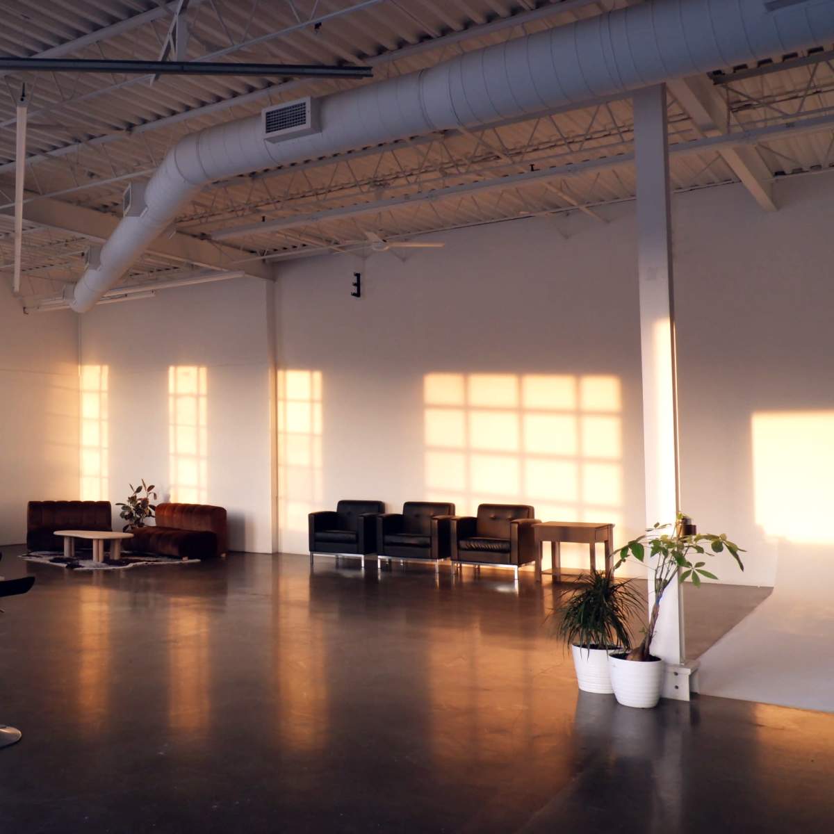 A spacious interior with large windows, polished concrete flooring, and a seating area featuring dark chairs and a small table.