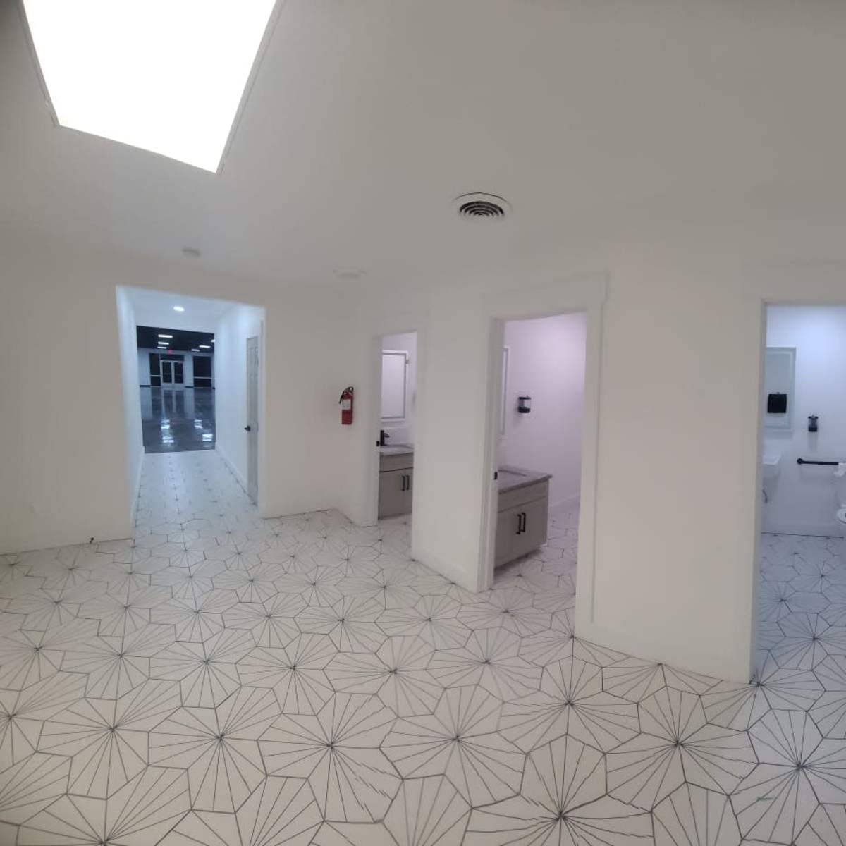 A light-filled corridor with white walls, a patterned floor, and three entrances to restrooms or utility rooms.