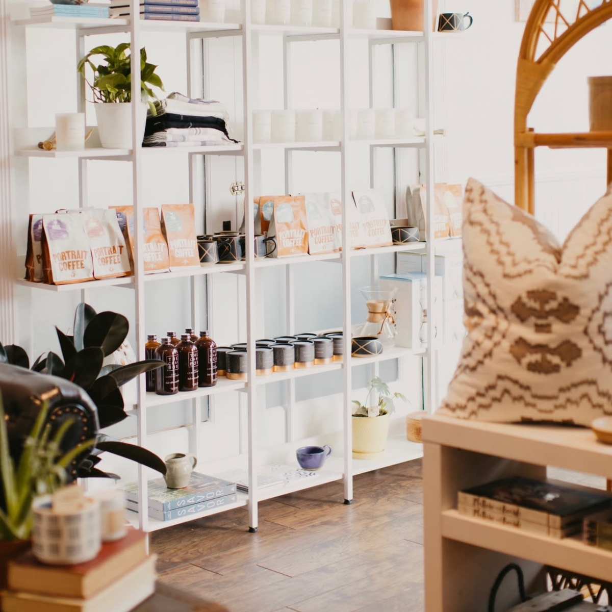 A neatly organized display of shelves featuring plants, candles, and various packaged items in a brightly lit room.