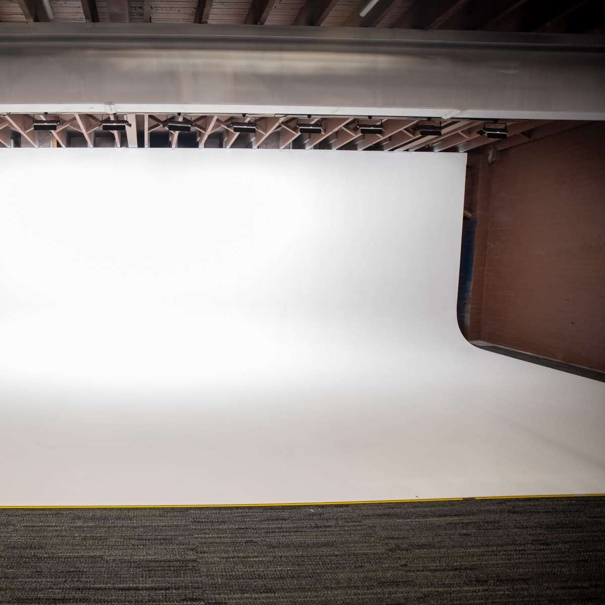A spacious photography studio featuring a large, seamless white backdrop and a soft carpeted floor.