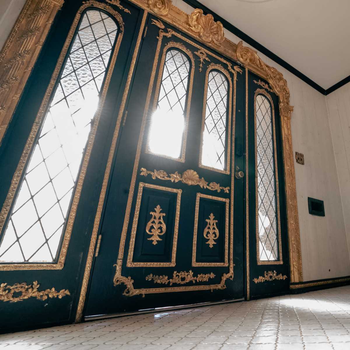 An ornate entrance with a pair of black double doors featuring decorative gold trim and a mirror on a small table beside them.