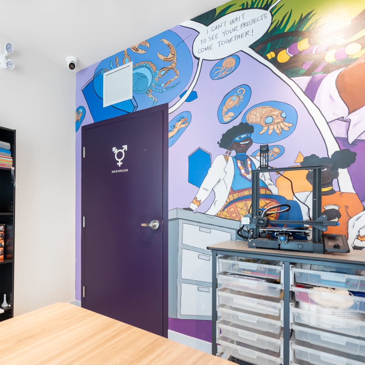 A modern room featuring a colorful mural on one wall, a purple door, and a black shelving unit filled with various items.