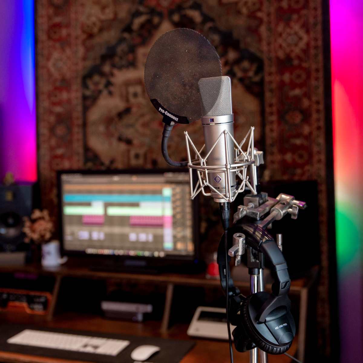 A microphone is positioned in front of a computer monitor displaying audio editing software in a recording studio.