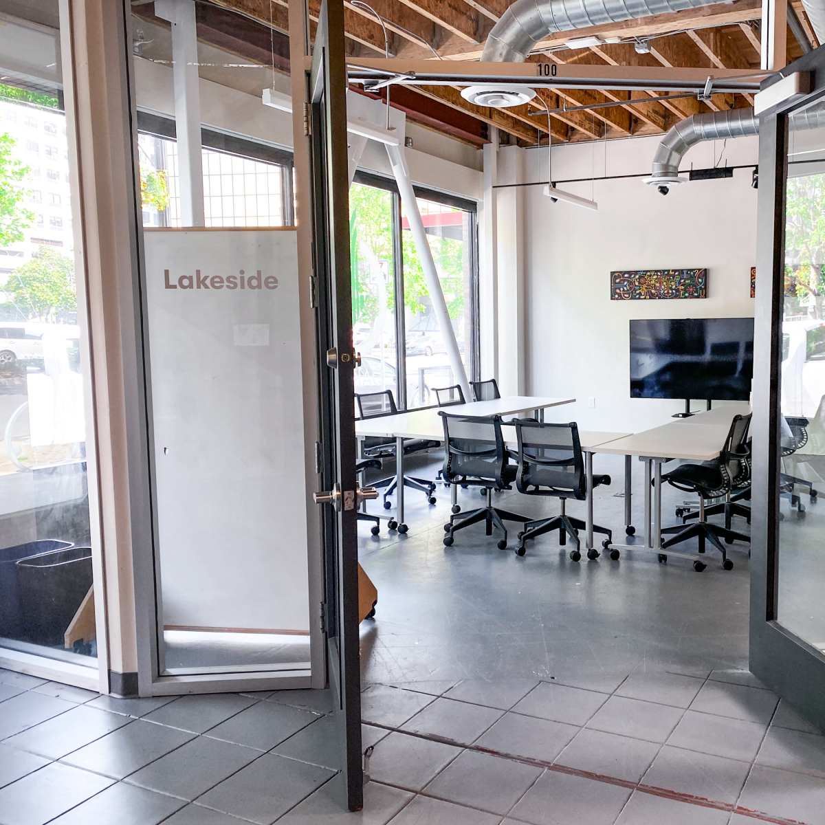 A modern meeting room with glass doors, equipped with a table, chairs, and a wall-mounted television.