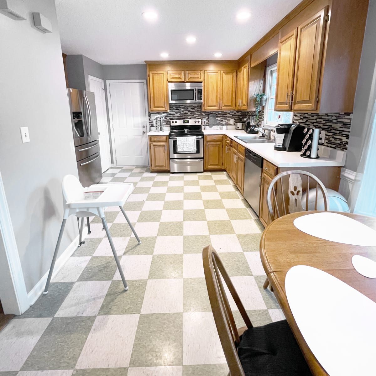 A modern kitchen with wooden cabinets, stainless steel appliances, and a checkered floor.