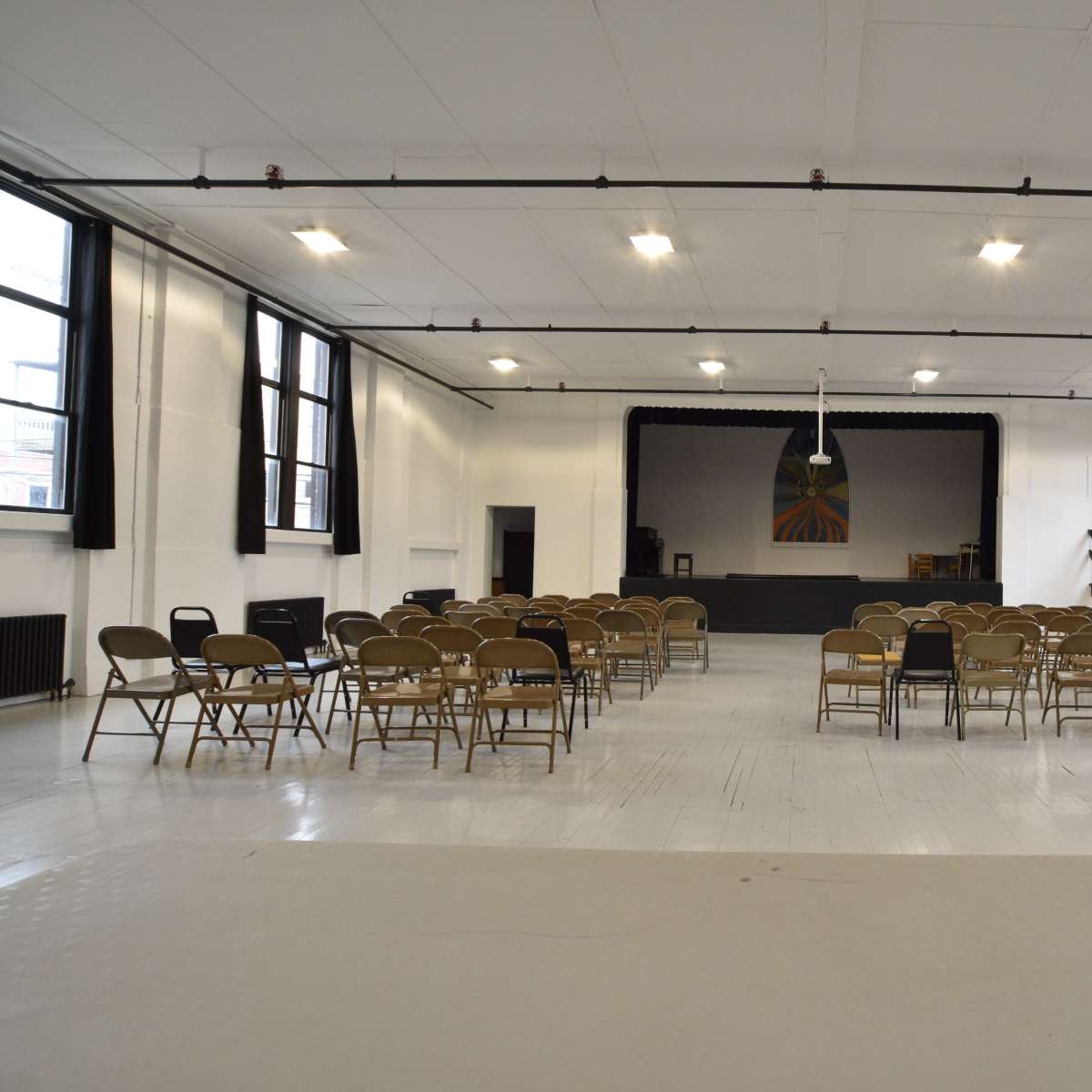 A large, empty hall with rows of folding chairs arranged facing a stage in front.