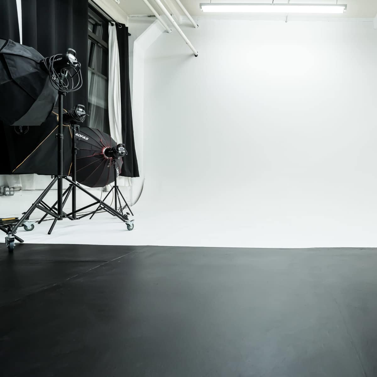 A photography studio with a white backdrop and a black floor, equipped with lighting and equipment on the left.