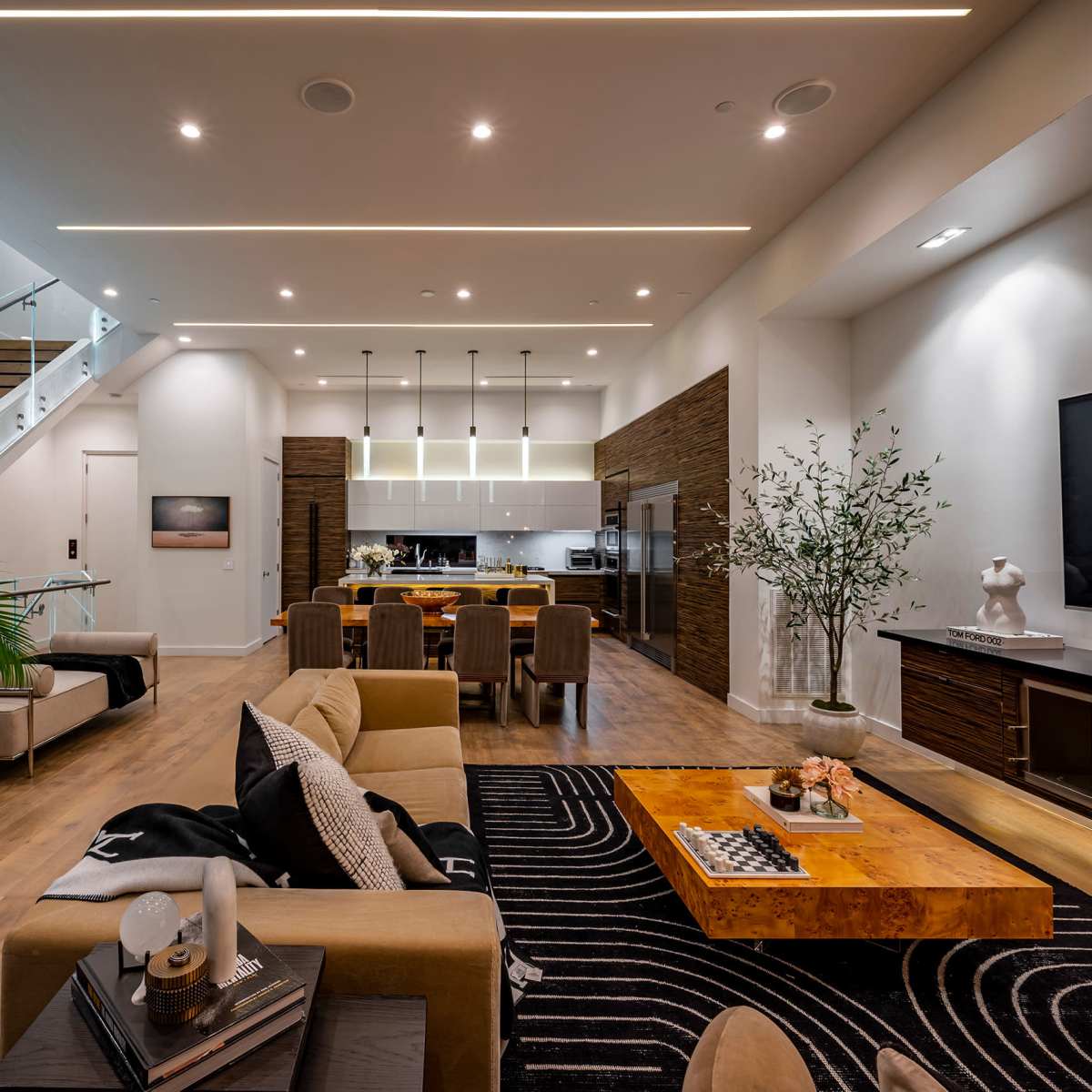 A modern living space featuring a kitchen, dining area, and a comfortable sitting area with a large coffee table and decorative plants.