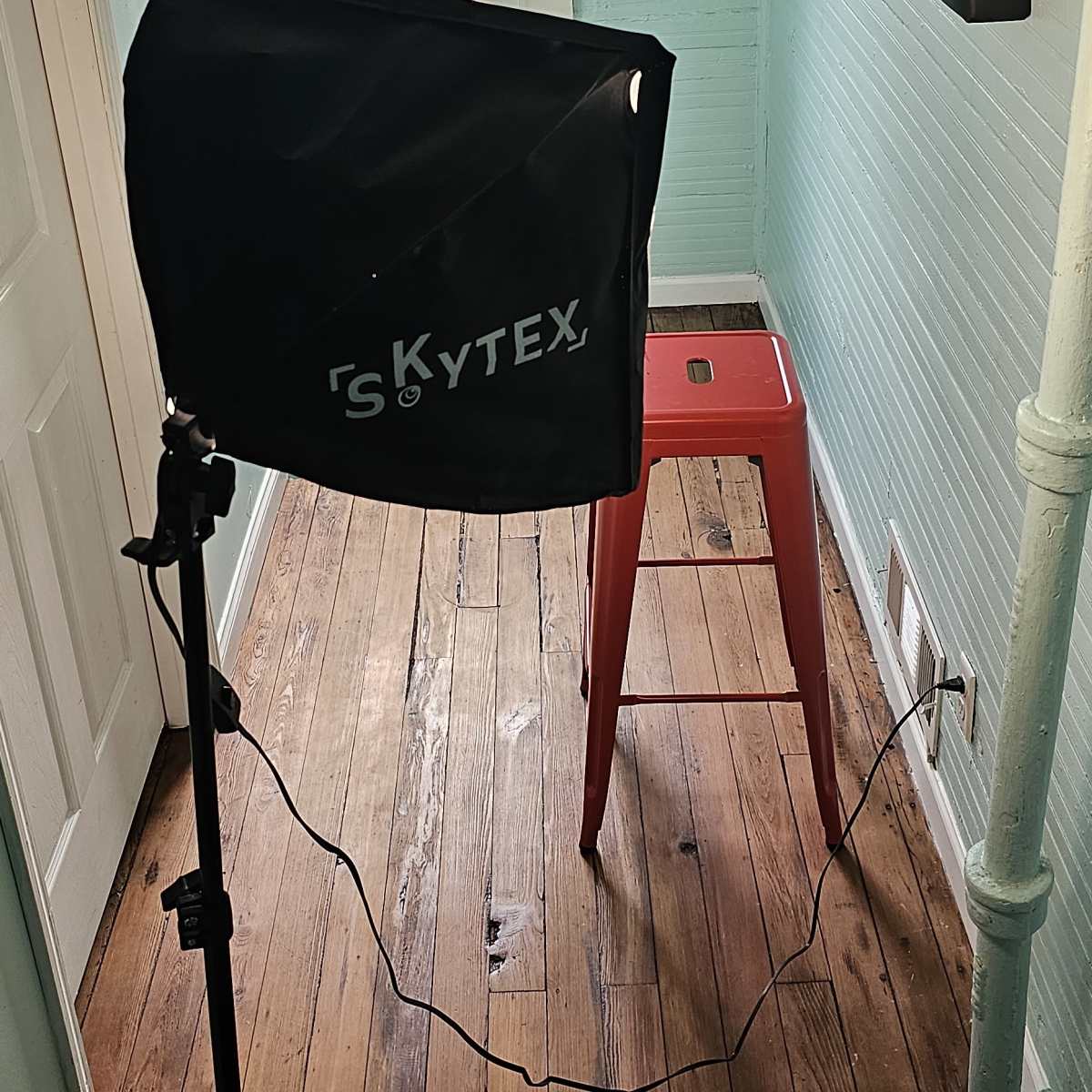 A studio setup features a light umbrella and a red stool positioned in a room with mint green walls and a window.