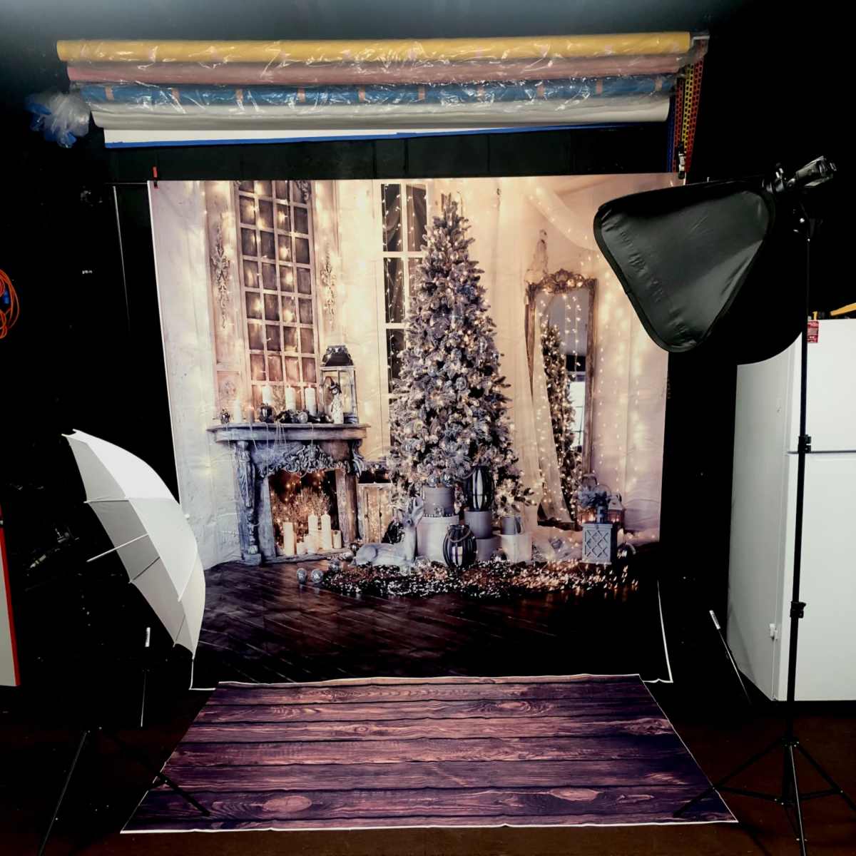 A photography setup featuring a decorated backdrop of a cozy room with a Christmas tree, flanked by two softbox lights on either side.