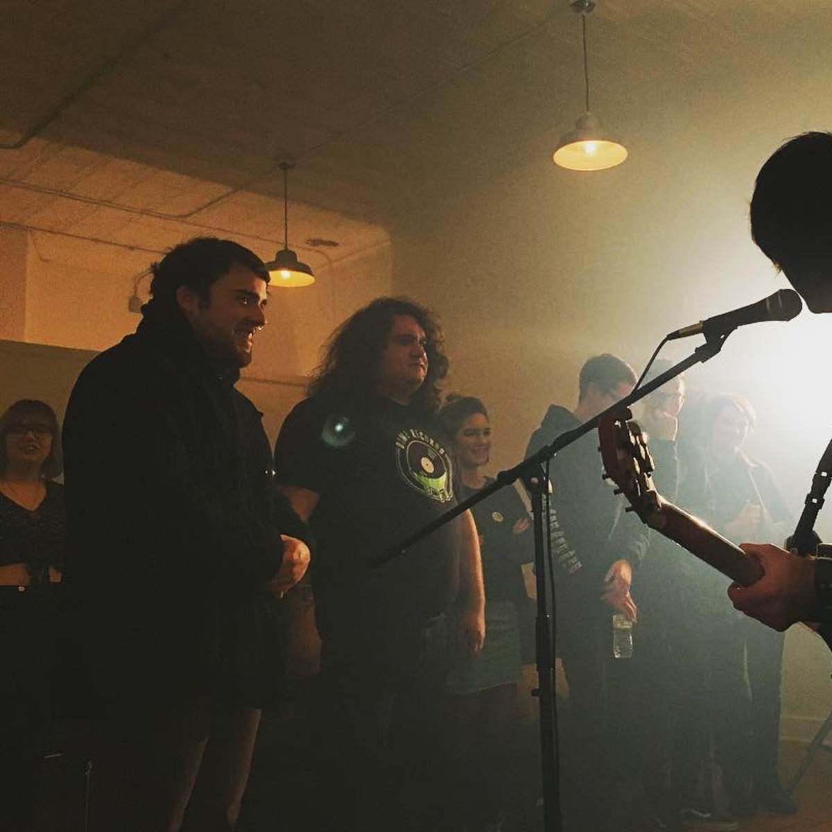 A musician performs on stage while an audience watches intently in a dimly lit room.