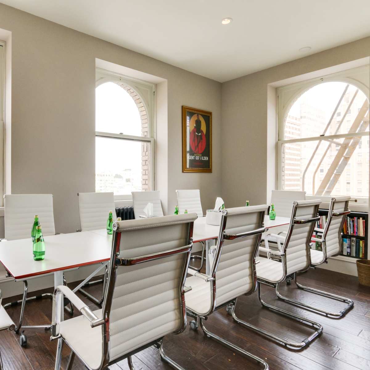 A modern meeting room features a long table surrounded by white chairs, with large windows that provide a view of the city.