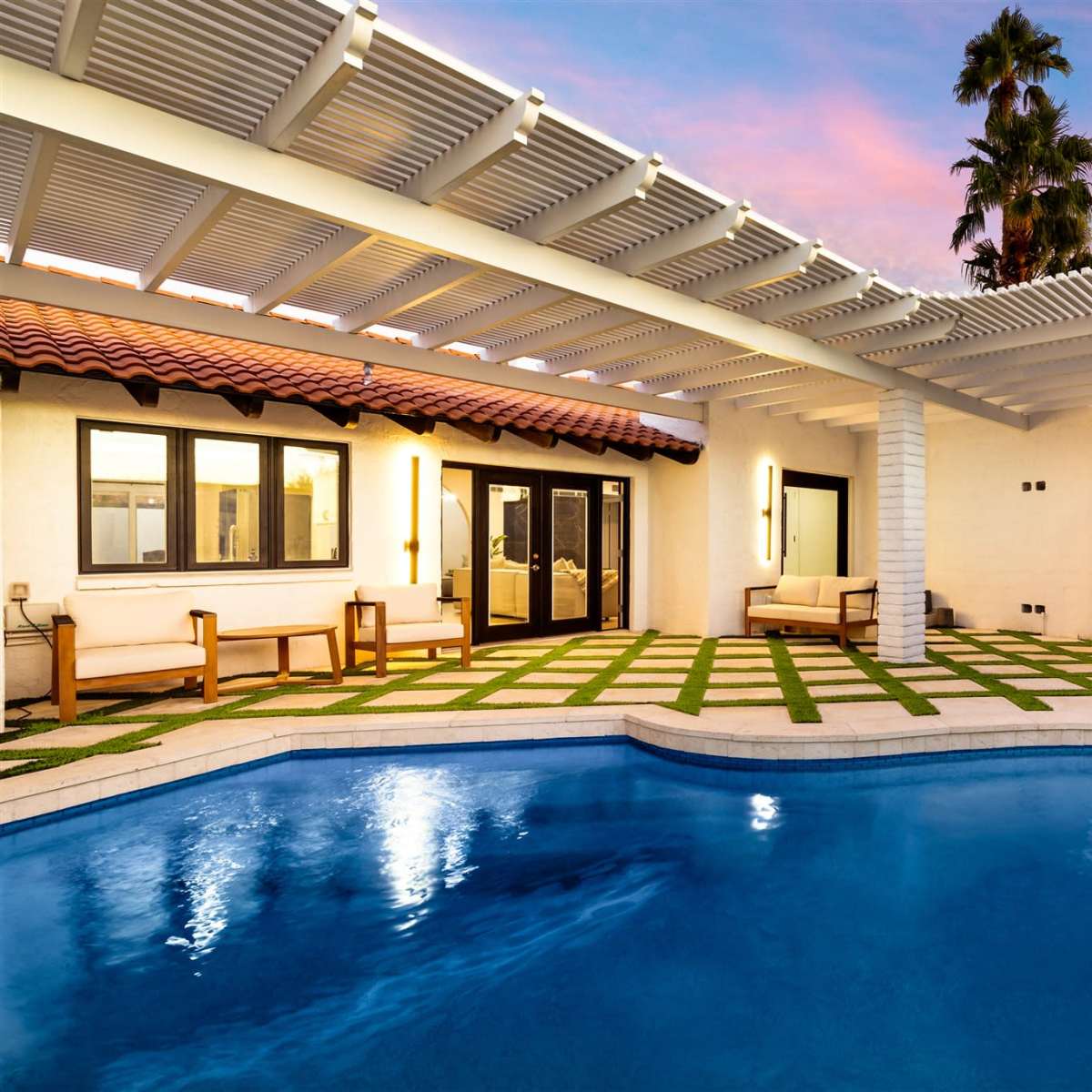 A backyard with a swimming pool surrounded by artificial grass, outdoor furniture, and a shaded area featuring a tent.
