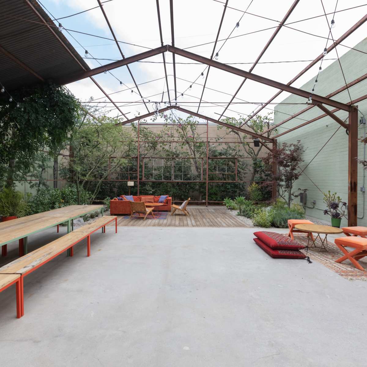 An open, industrial-style space with wooden benches, colorful seating arrangements, and greenery surrounding a wooden deck area.