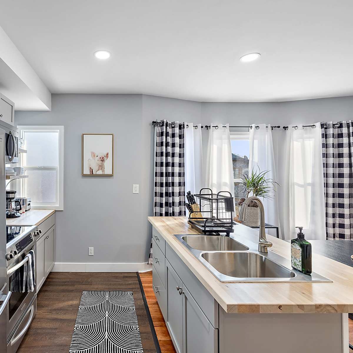 A modern kitchen features stainless steel appliances, a wooden countertop, and a large window with checkered curtains.