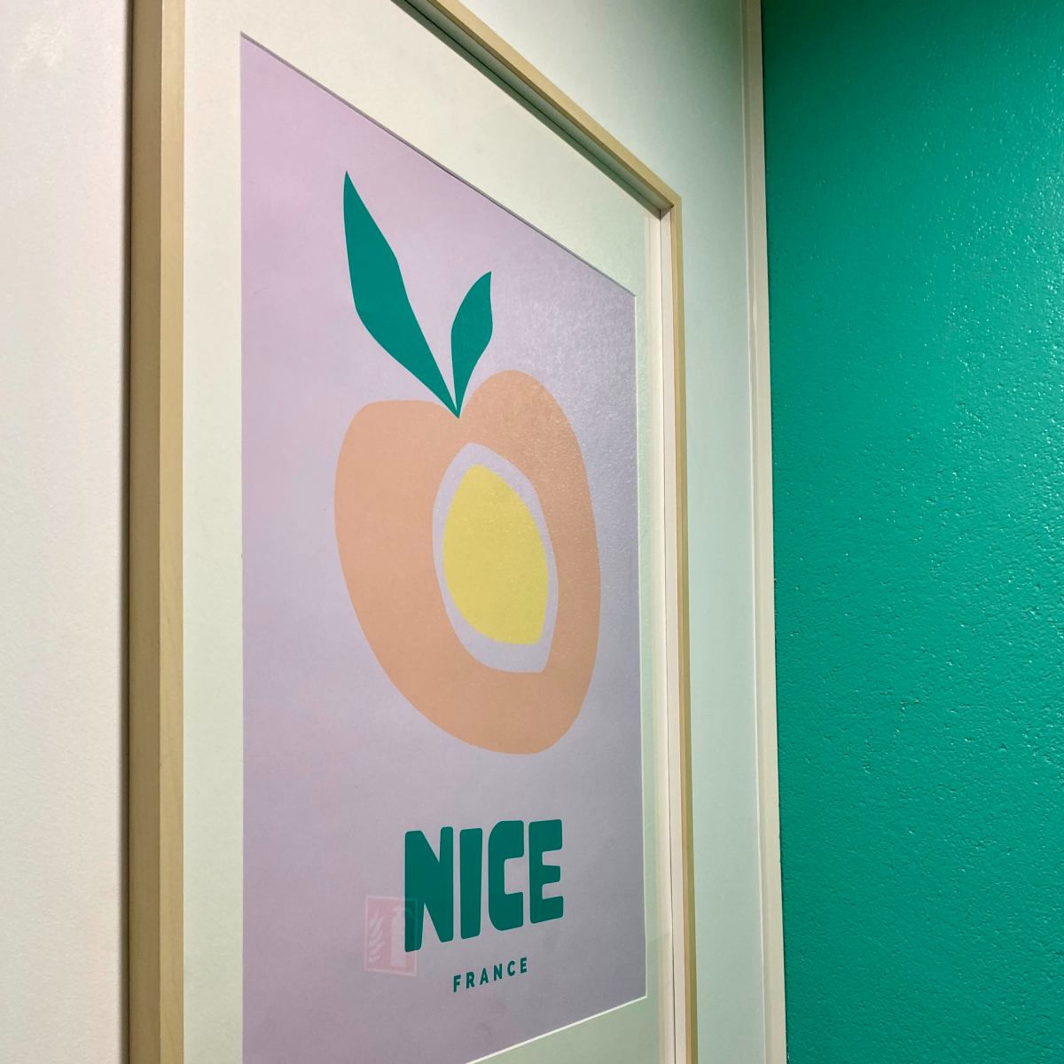 A framed poster featuring a stylized peach and the words "NICE FRANCE" against a light background, displayed on a wall painted in a vibrant green color.