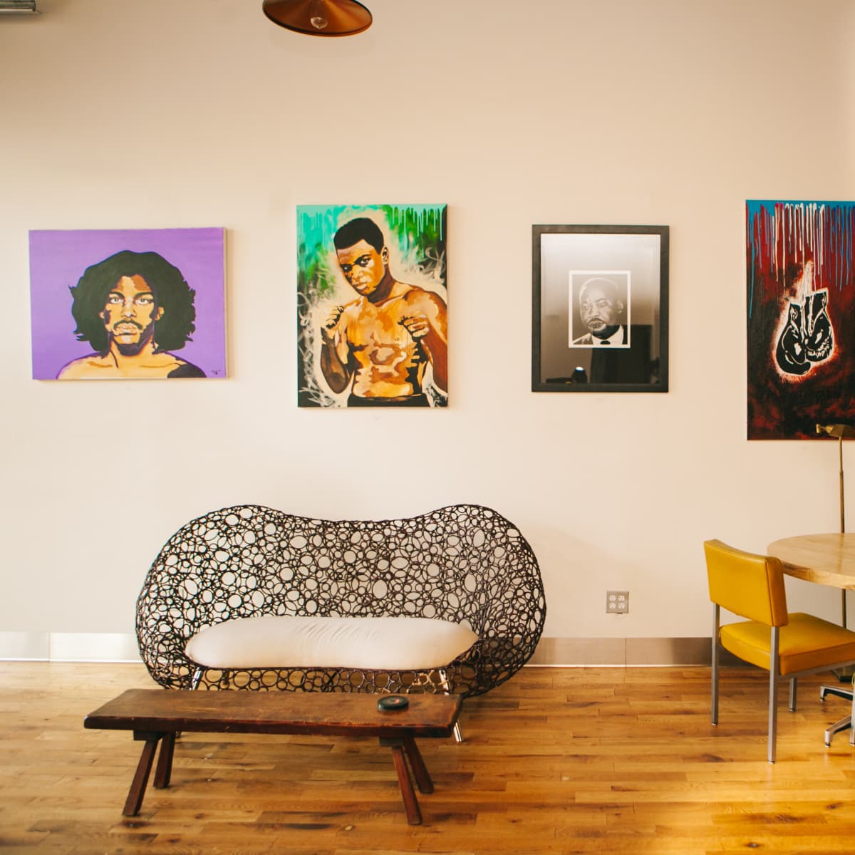 A modern café interior featuring an artistic wall with vibrant paintings of musicians and a cozy seating area with a round table and chairs.