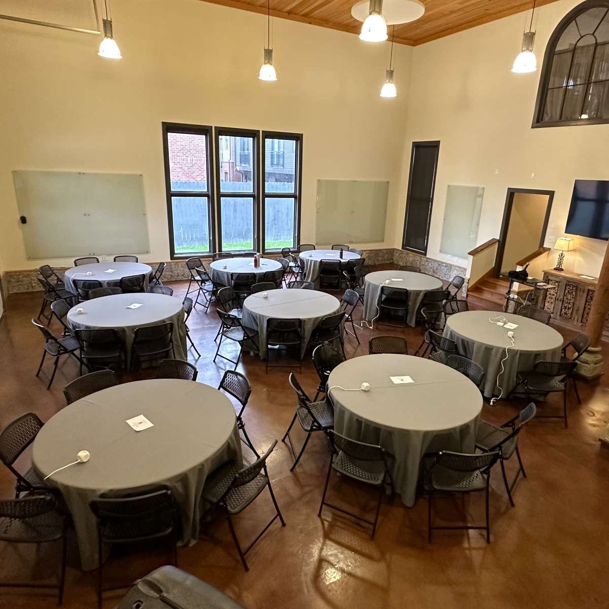 A large, well-lit room arranged with several round tables covered in gray tablecloths and surrounded by black chairs.
