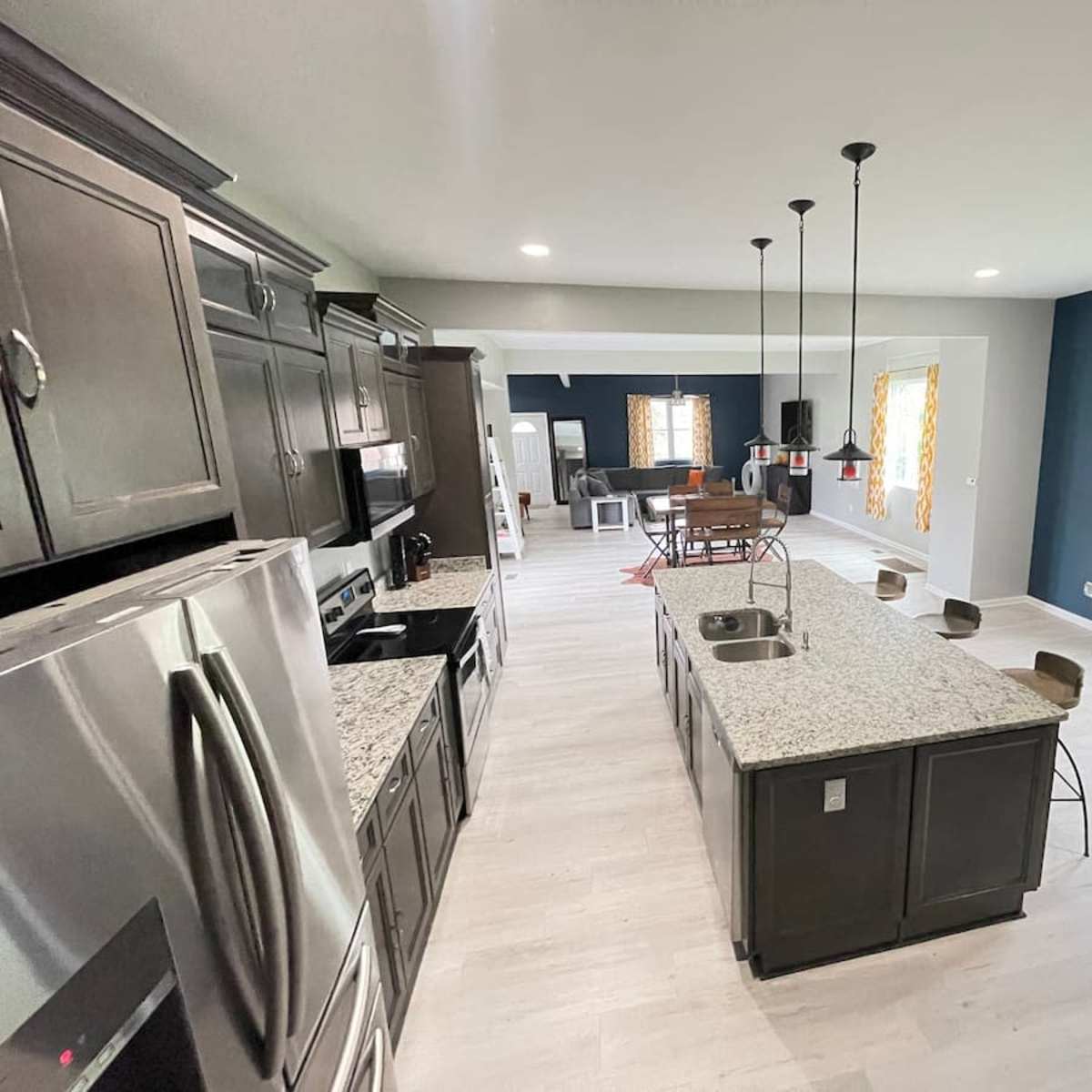 A modern kitchen featuring dark cabinetry, granite countertops, and an island with seating, open to a dining area with a table and chairs.